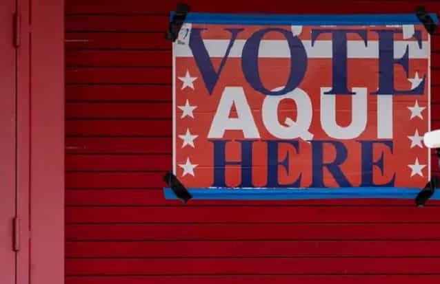 Letrero detras de una cortina metalica roja que dice VOTE AQUI
